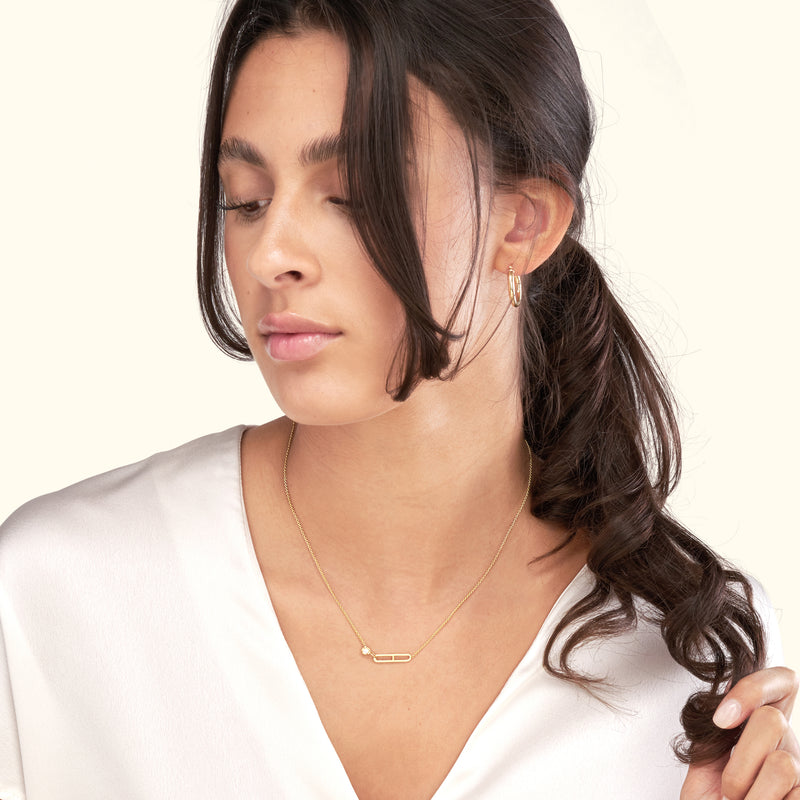 Gold necklace and earrings worn by a woman with long, dark hair, against a light background.