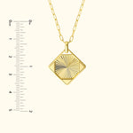 Gold pendant necklace with a diamond-shaped design and textured surface, beside a ruler for size.