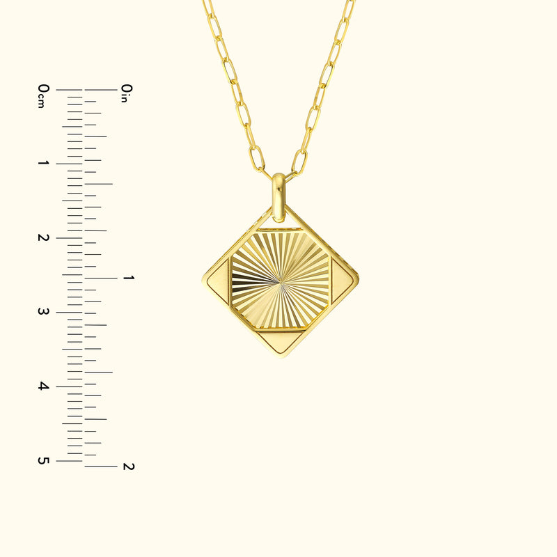 Gold pendant necklace with a diamond-shaped design and textured surface, beside a ruler for size.