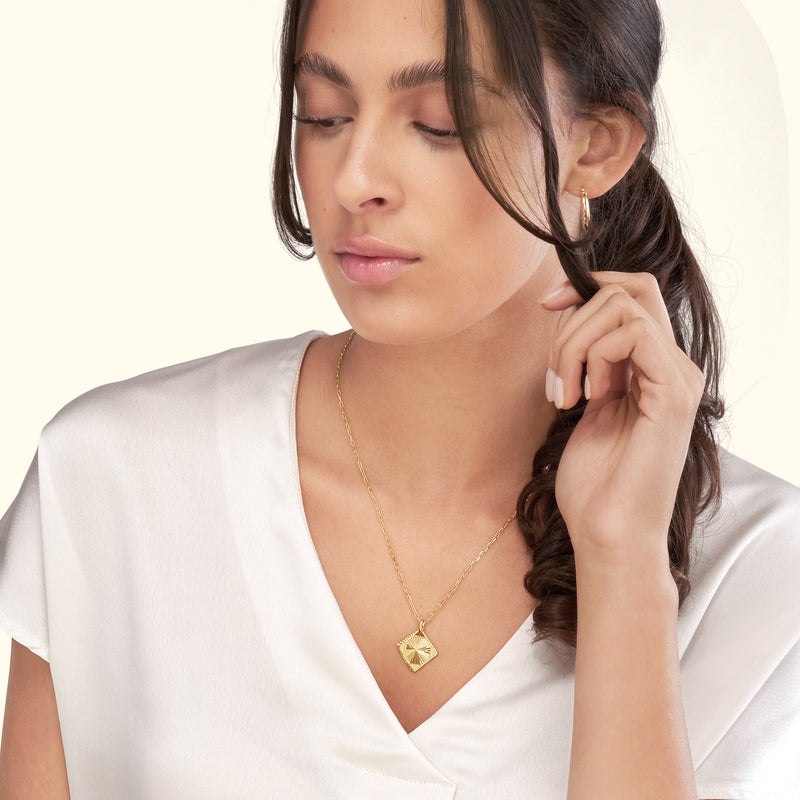 A woman wearing a gold necklace with a pendant, styled with a silk blouse.