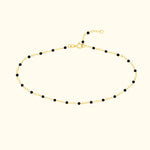 Delicate gold bracelet with black beads, featuring a clasp and adjustable chain.