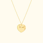 Shiny gold heart pendant on a delicate chain against a light background.
