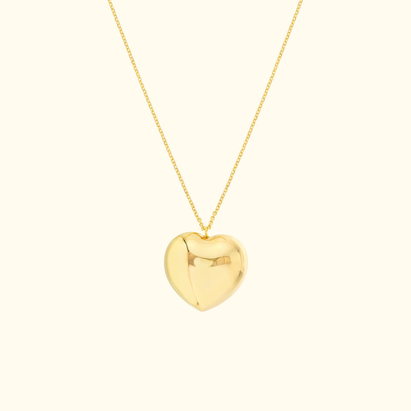 Shiny gold heart pendant on a delicate chain against a light background.