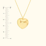 Gold heart-shaped pendant with a chain, displayed alongside a ruler for scale.
