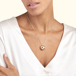 Gold heart pendant necklace worn by a woman in a silky white blouse.
