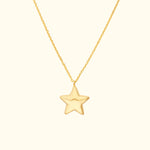 Gold star pendant necklace on a delicate chain against a light background.