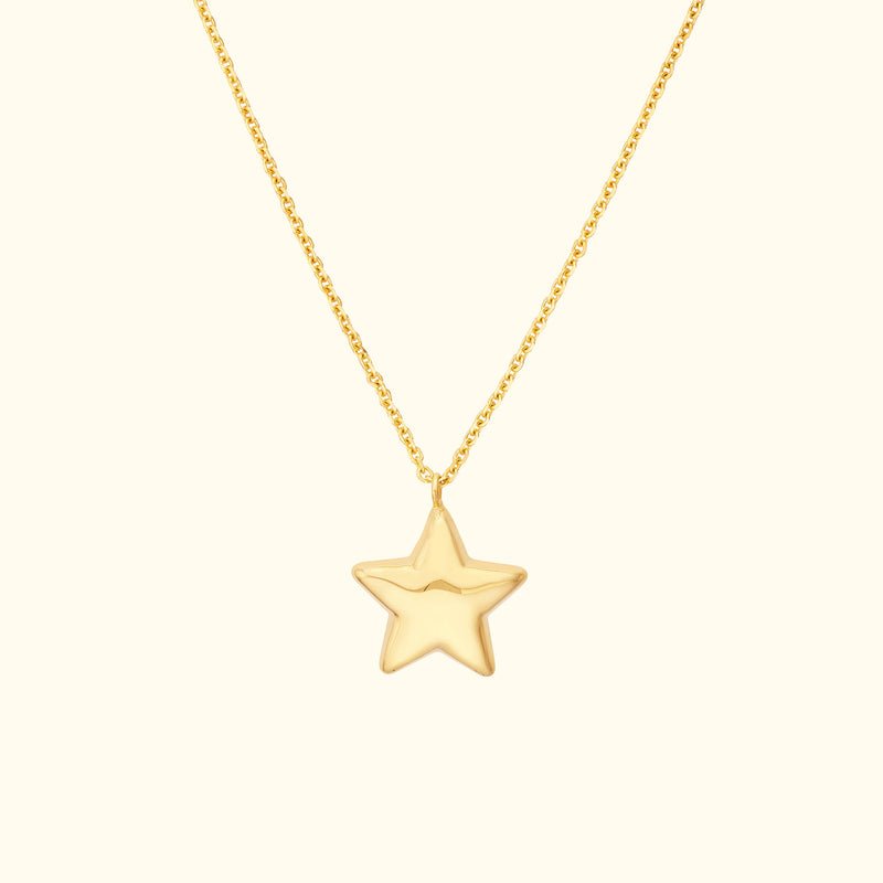 Gold star pendant necklace on a delicate chain against a light background.