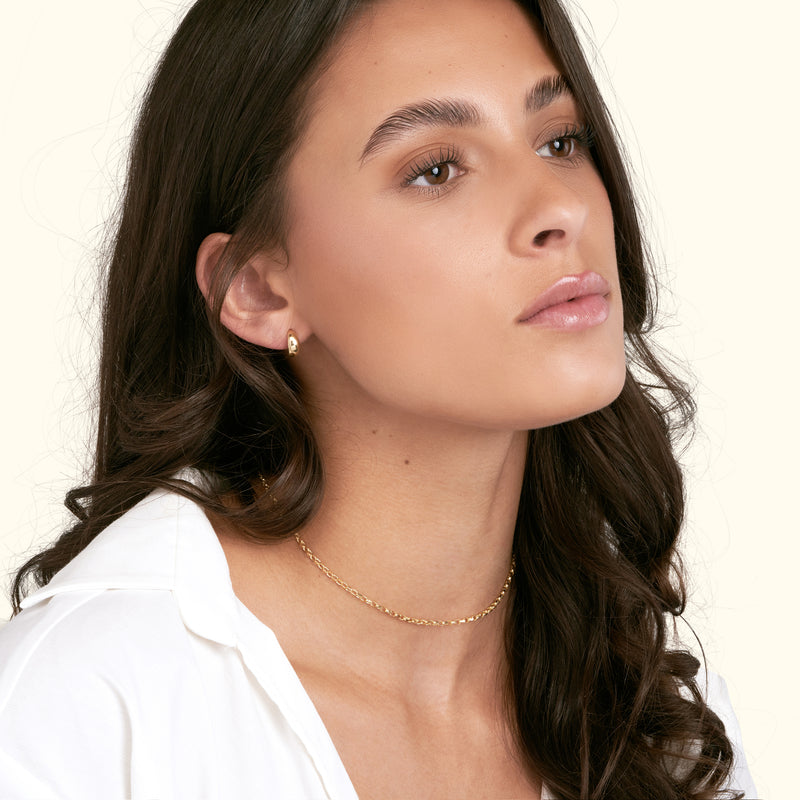 Model wears a delicate gold choker and small earrings, with a serene expression.