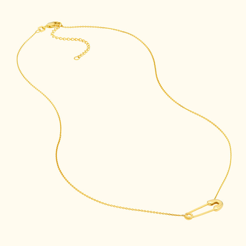 Delicate gold necklace featuring a safety pin charm.