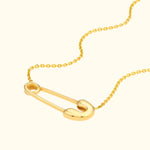Gold necklace featuring a large safety pin pendant on a delicate chain.