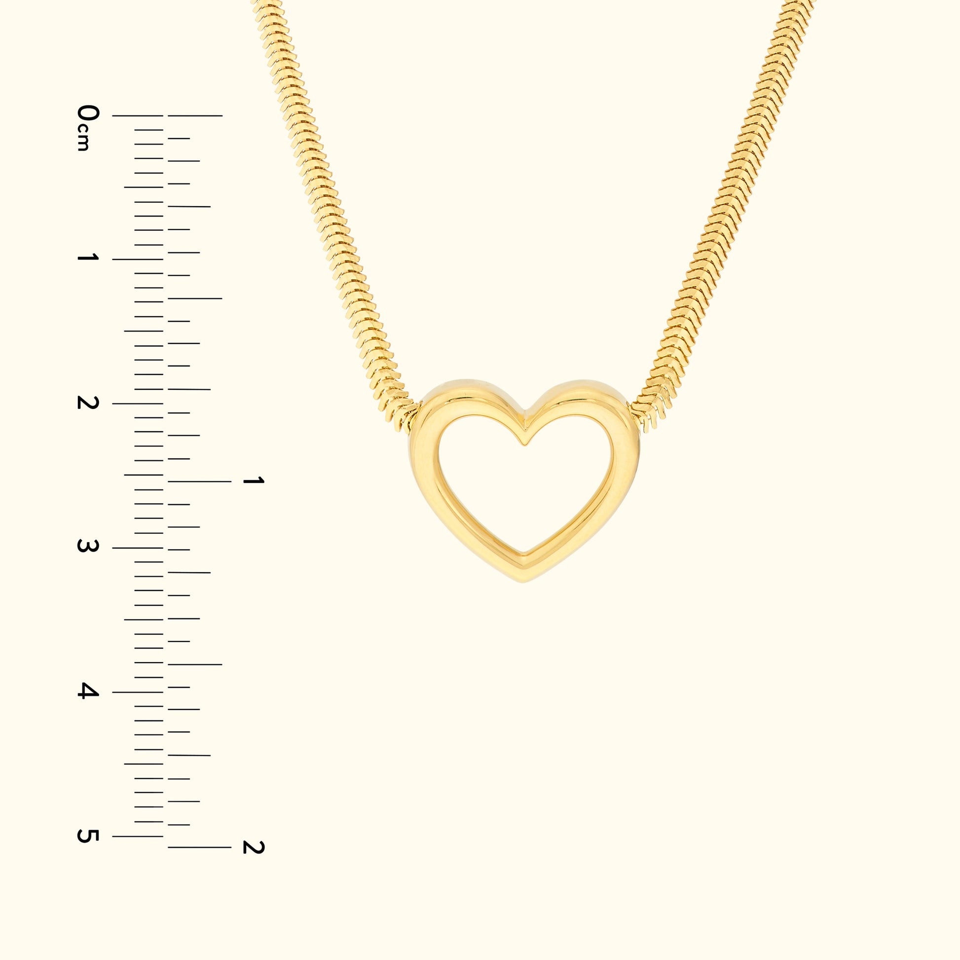 Gold heart pendant necklace on a smooth background, with a ruler for size reference.