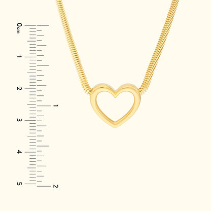 Gold heart pendant necklace on a smooth background, with a ruler for size reference.