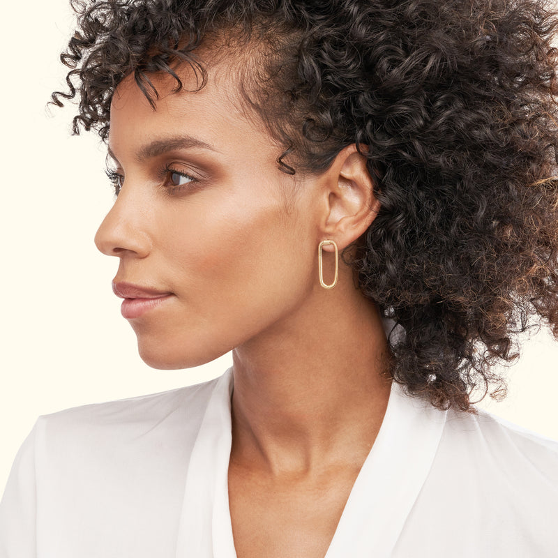 Gold geometric hoop earring worn by a woman with curly hair, in profile.