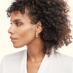 Gold hoop earrings worn by a woman with curly hair, against a light background.