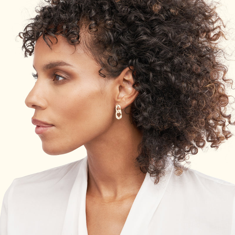 Gold hoop earrings worn by a woman with curly hair, against a light background.