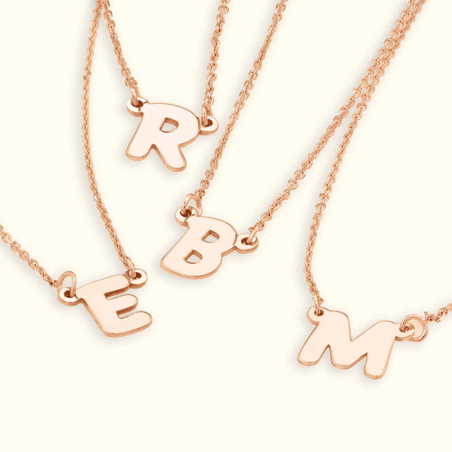 Rose gold necklaces featuring initials R, E, B, and M on delicate chains.