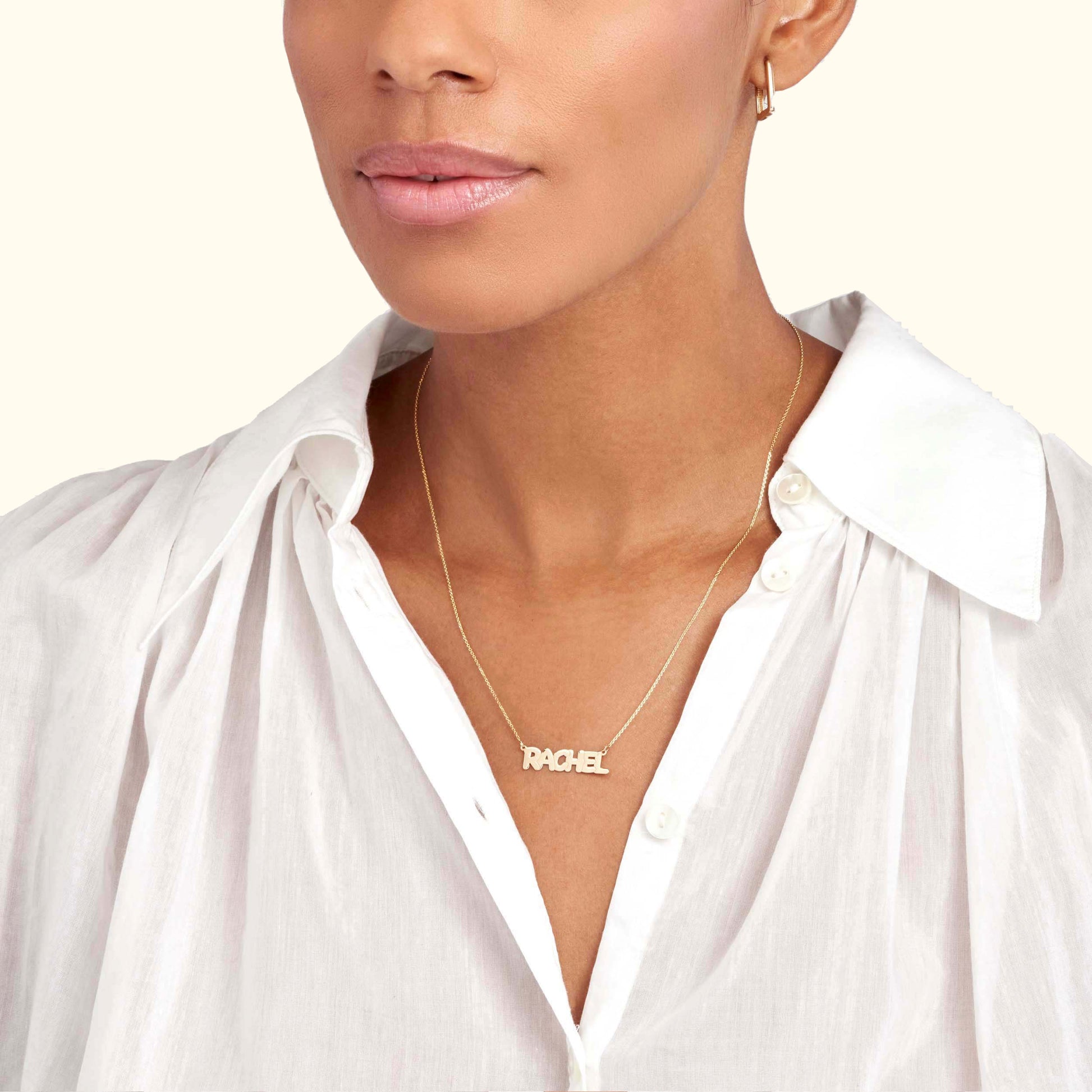 Gold name necklace worn over a white blouse, with a close-up of the model's face.