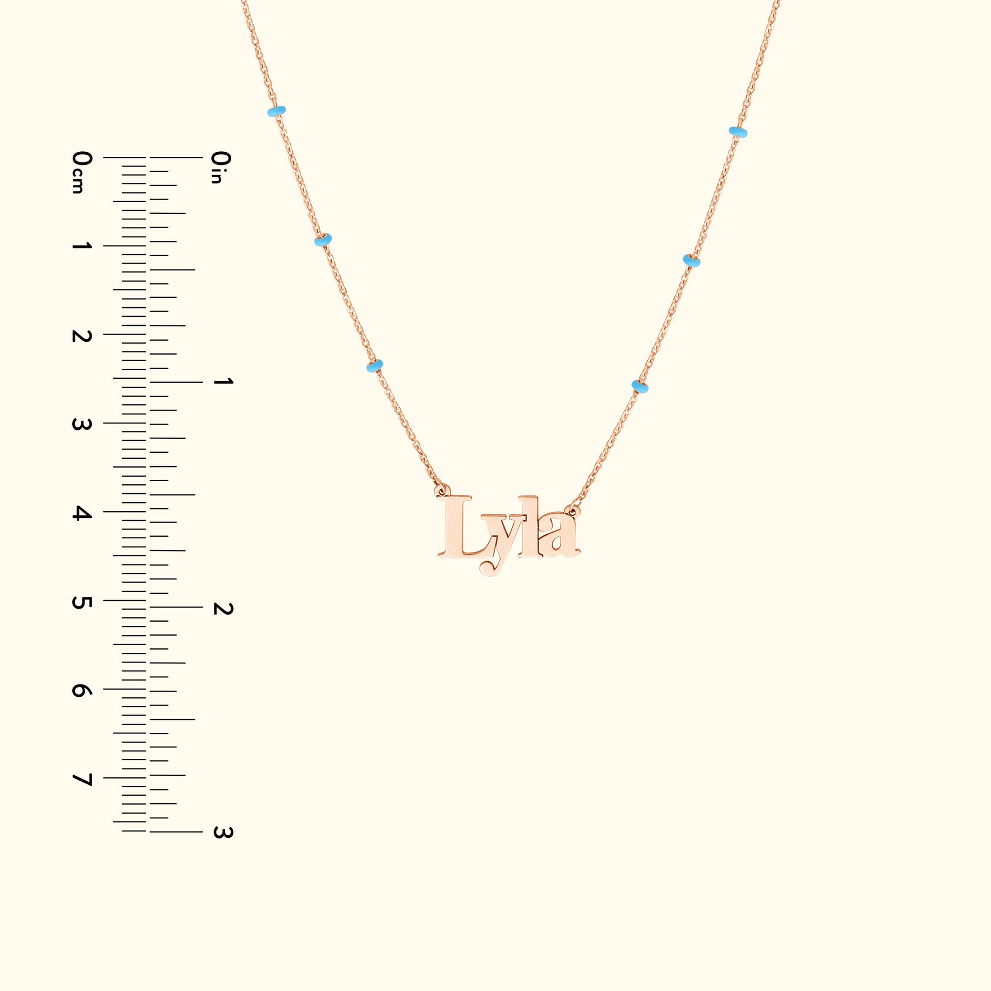 Rose gold necklace with the name "Lyla" and small turquoise beads, paired with a ruler for size reference.