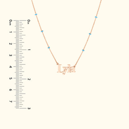 Rose gold necklace with the name "Lyla" and small turquoise beads, paired with a ruler for size reference.