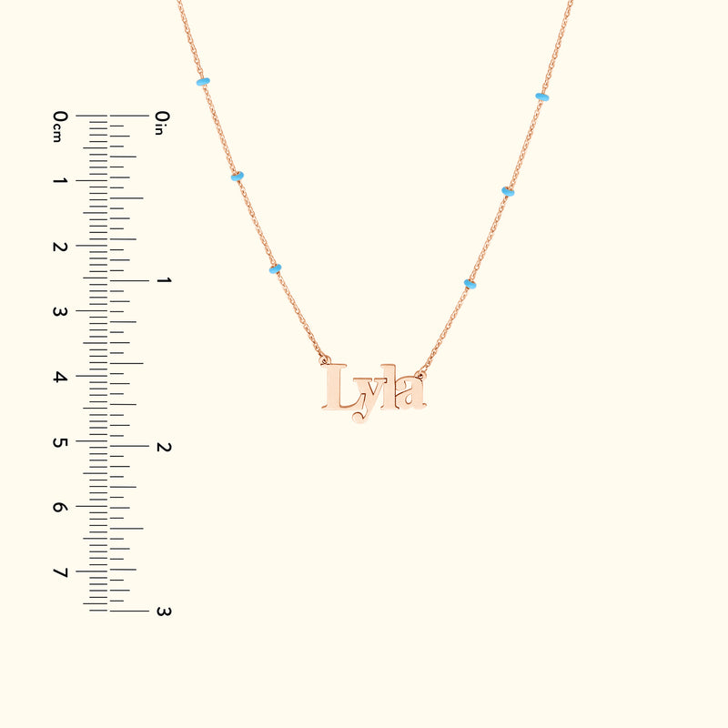 Rose gold necklace with the name "Lyla" and small turquoise beads, paired with a ruler for size reference.