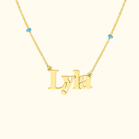 Gold necklace with the name "Lyla" and small turquoise beads on each side.