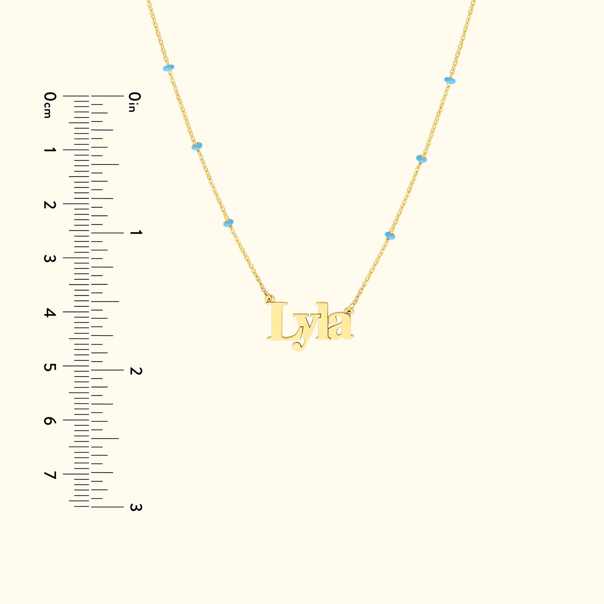 Gold necklace featuring the name "Lyla" with blue accents and a ruler for scale.