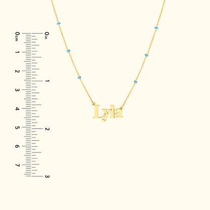 Gold necklace featuring the name "Lyla" with blue accents and a ruler for scale.