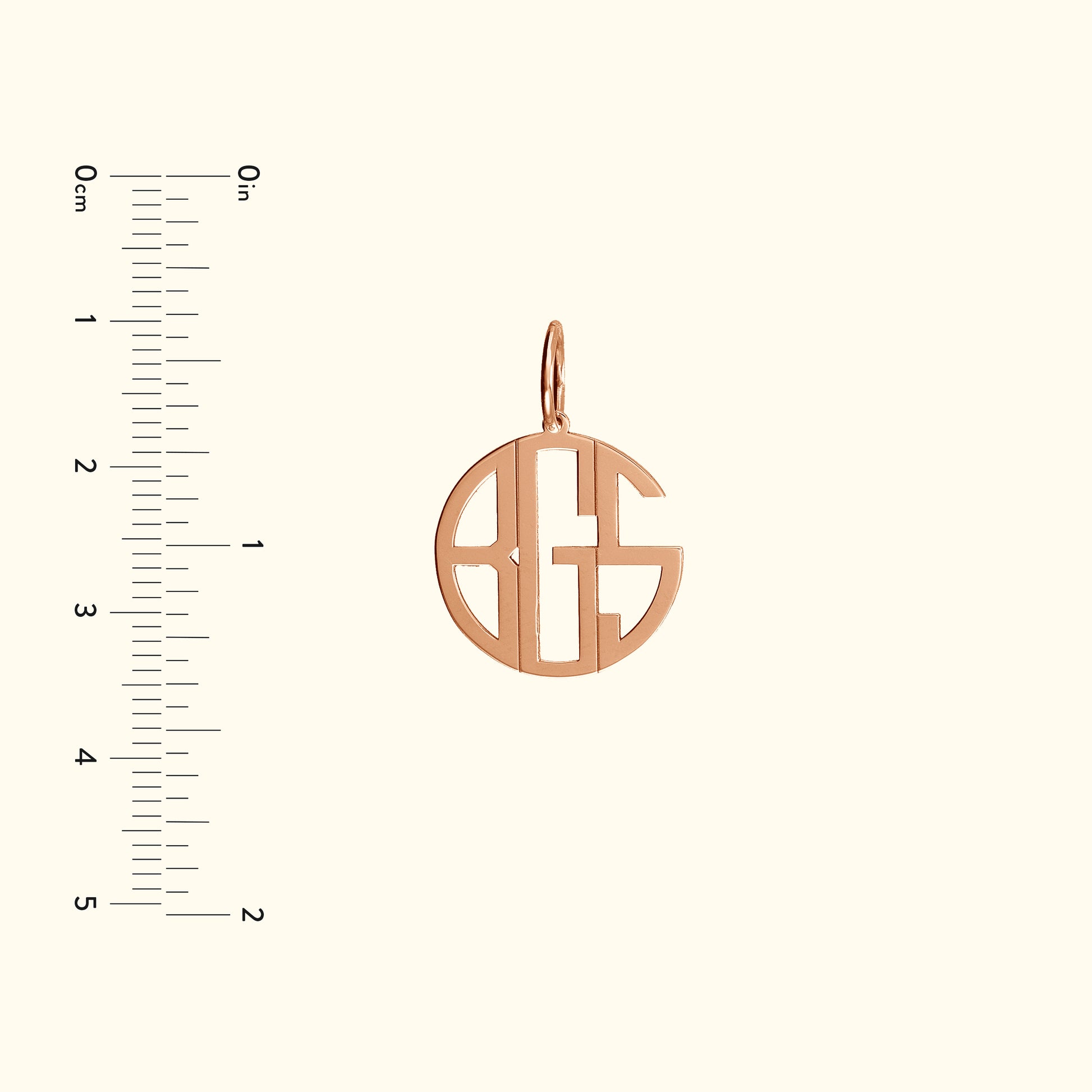 Rose gold monogram pendant with an open design, accompanied by a ruler for size reference.