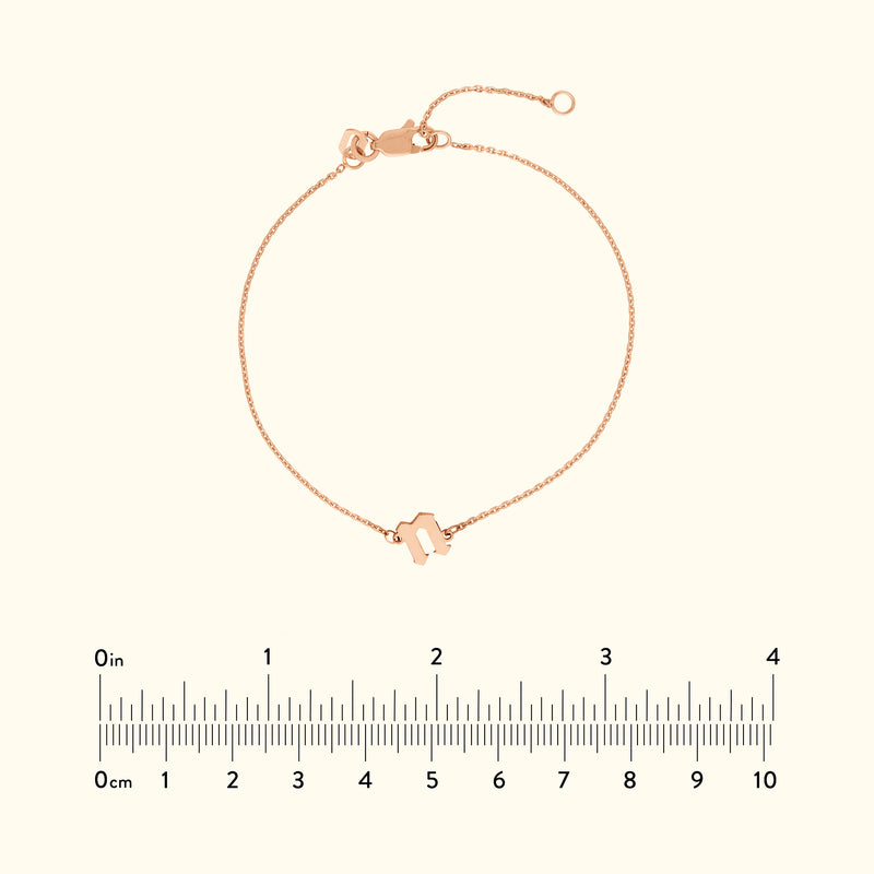 Delicate rose gold bracelet with a geometric charm, displayed with a ruler for size reference.