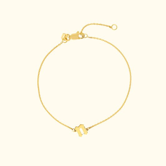 Delicate gold bracelet with a unique charm on a light background.