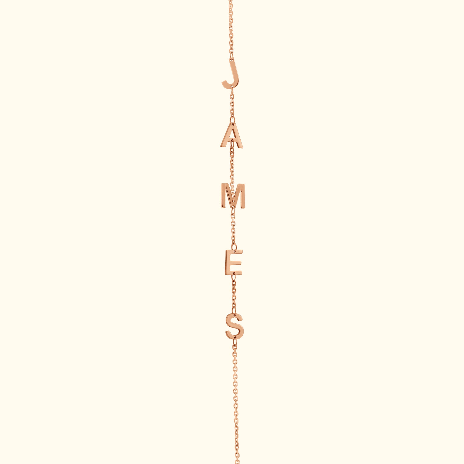 Rose gold necklace with letters spelling "JAMES" hanging from a delicate chain.