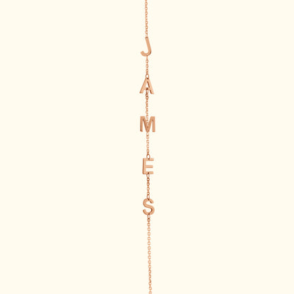 Rose gold necklace with letters spelling "JAMES" hanging from a delicate chain.