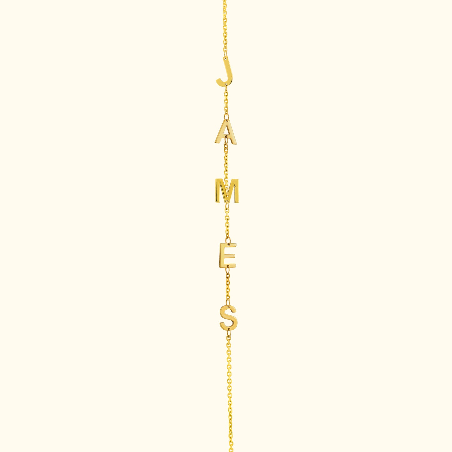 Gold necklace with letters spelling "JAMES" hanging from a delicate chain.