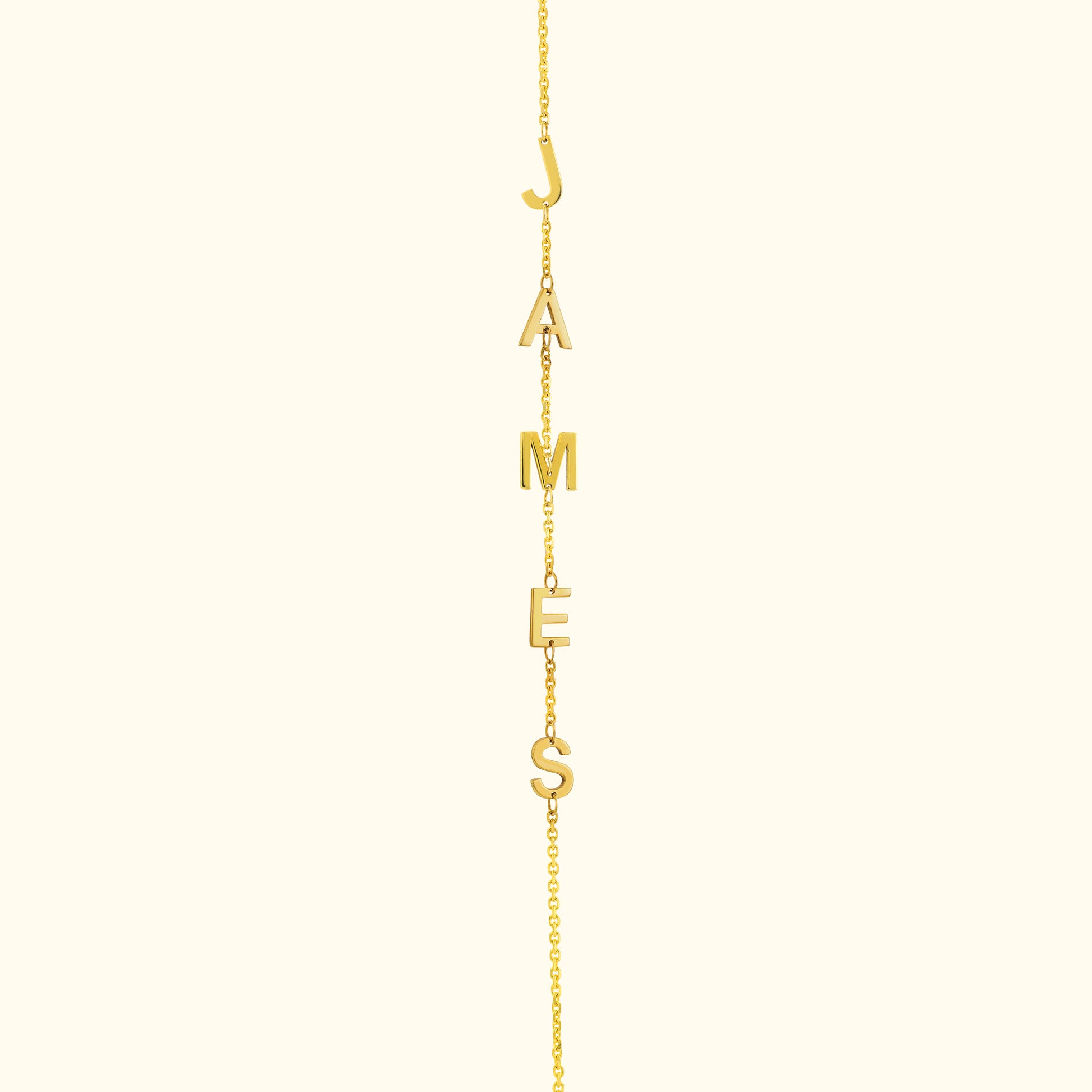 Gold necklace with letters spelling "JAMES" hanging from a delicate chain.