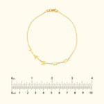 Gold bracelet featuring alphabet charms, displayed with a ruler for size reference.