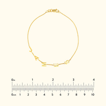 Gold bracelet featuring alphabet charms, displayed with a ruler for size reference.