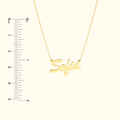 Gold necklace featuring the name "Sofia" in a cursive font, with a ruler for scale.