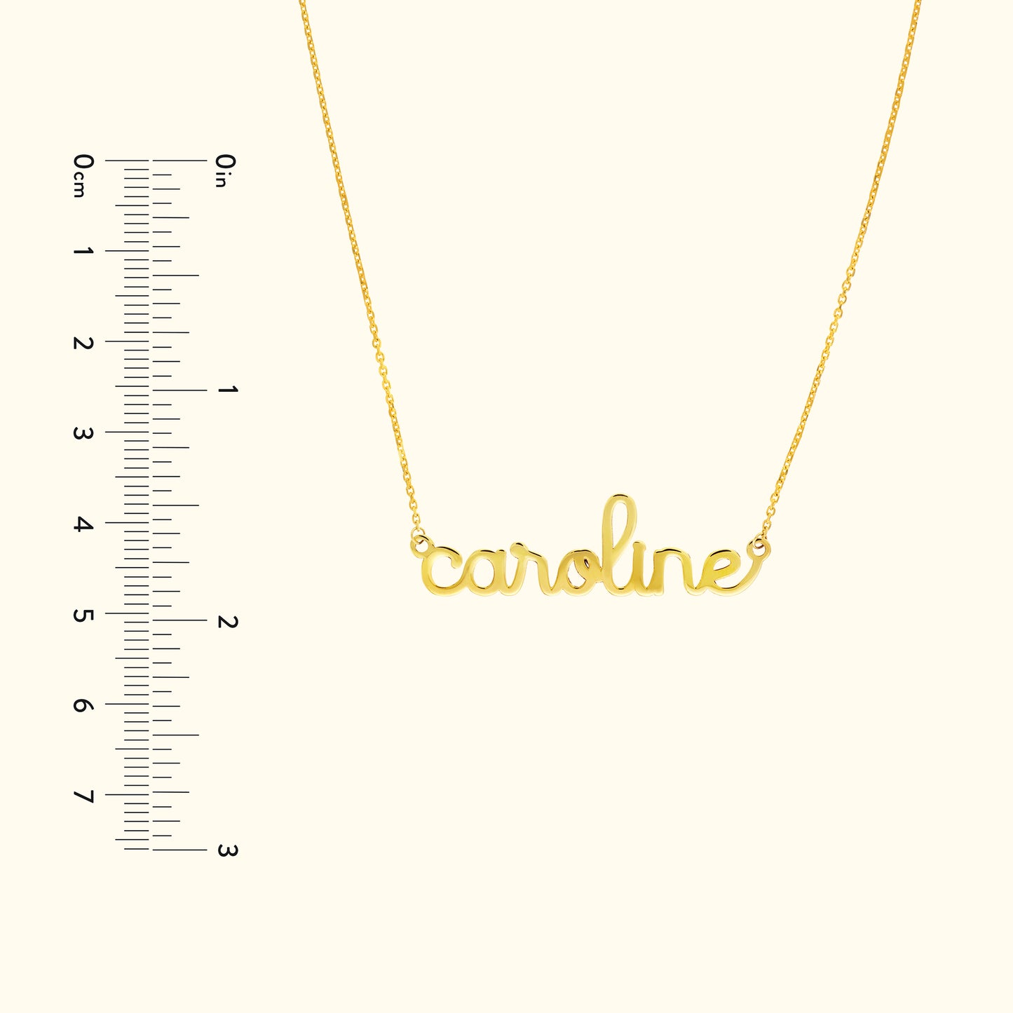 Gold necklace with the name "caroline" in cursive script, alongside a ruler for scale.