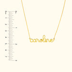 Gold necklace with the name "caroline" in cursive script, alongside a ruler for scale.