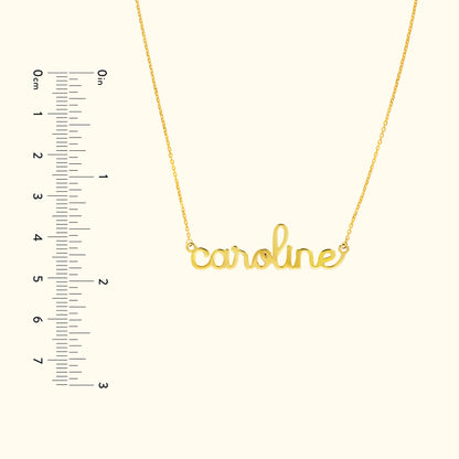 Gold necklace with the name "caroline" in cursive script, alongside a ruler for scale.