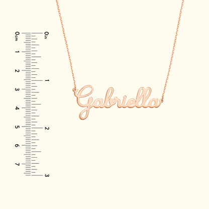 Rose gold necklace with the name "Gabriella" elegantly scripted, next to a ruler for size reference.