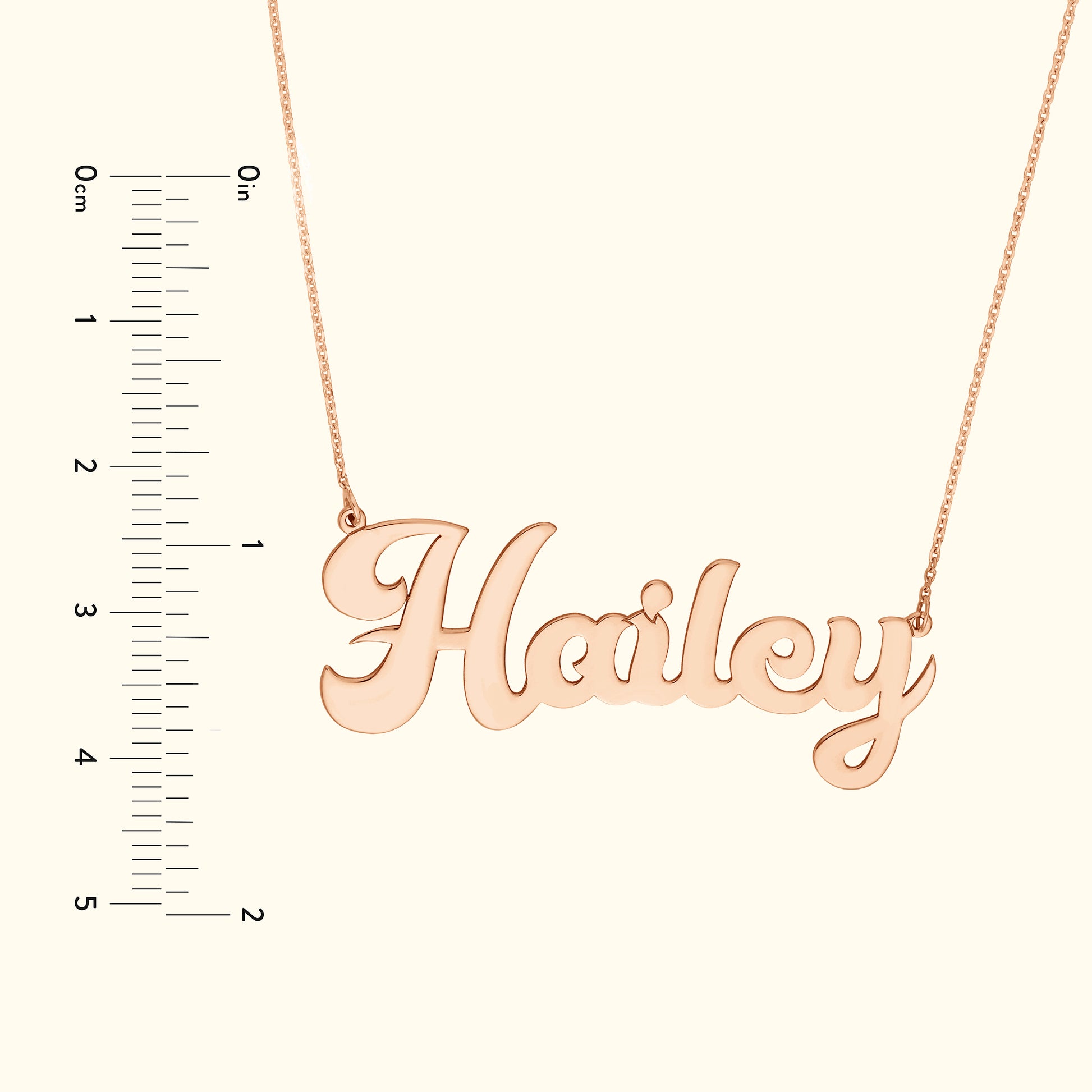 Rose gold name necklace reading "Hailey," alongside a ruler for size reference.