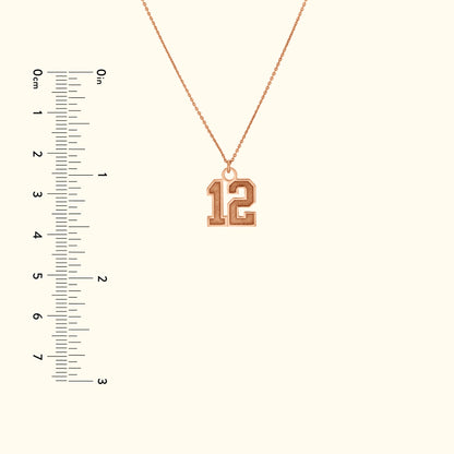 Rose gold necklace featuring a large "12" pendant, displayed with a ruler for size reference.