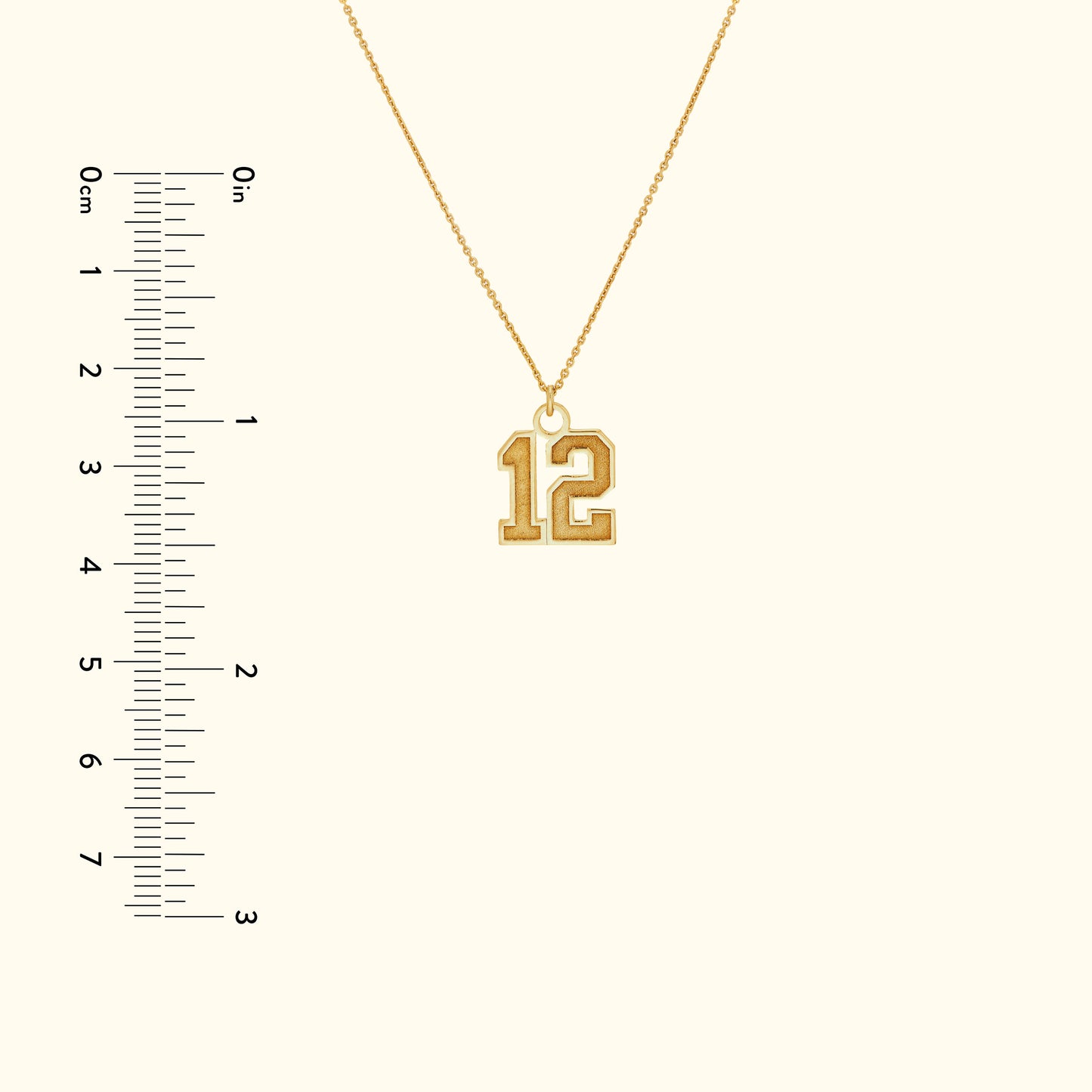 Gold necklace featuring a large, stylized number "12" pendant, with a ruler for size reference.