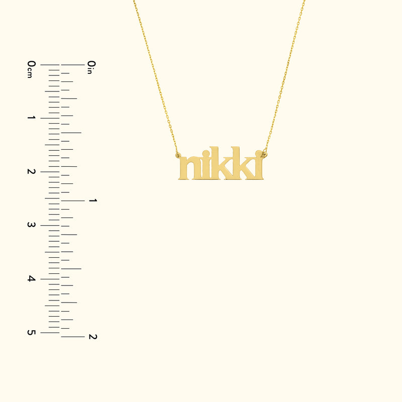 Gold necklace featuring the name "nikki" in a playful font, next to a ruler for scale.