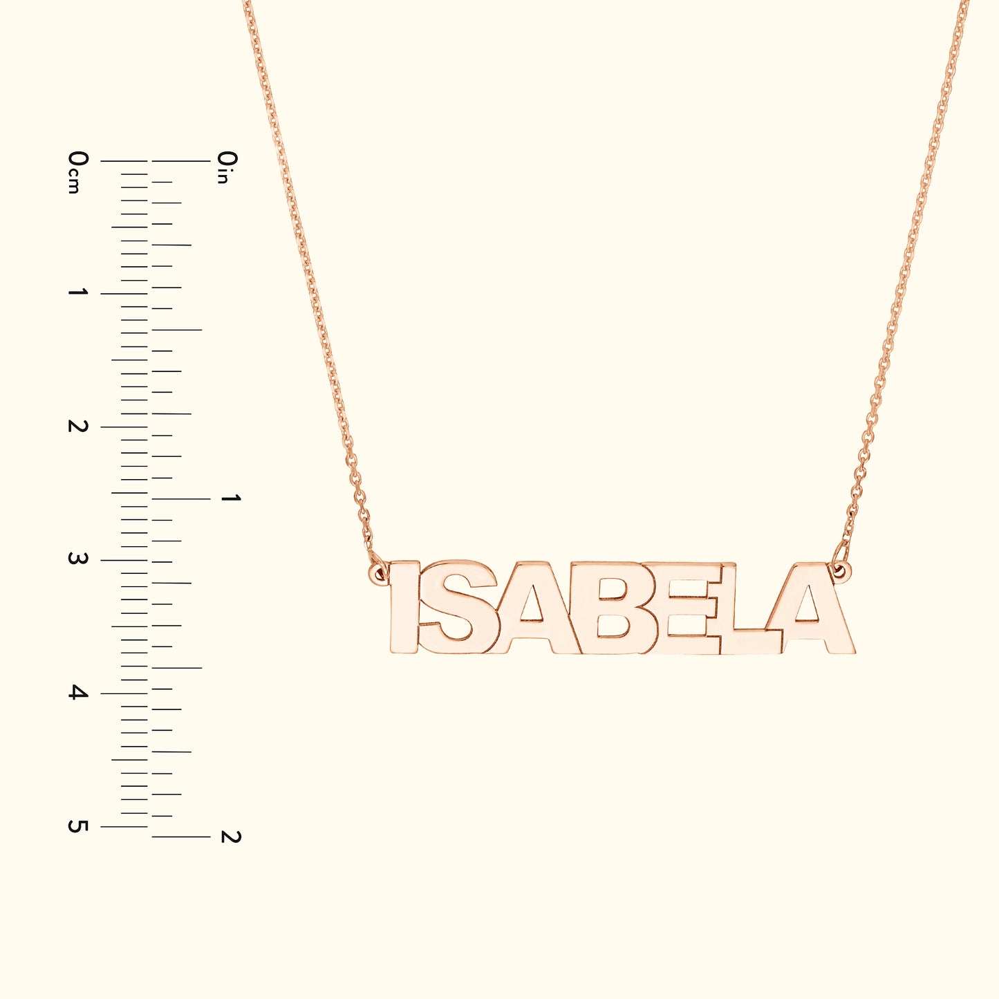 Rose gold necklace with the name "ISABELA" hanging on a delicate chain, alongside a ruler for size reference.