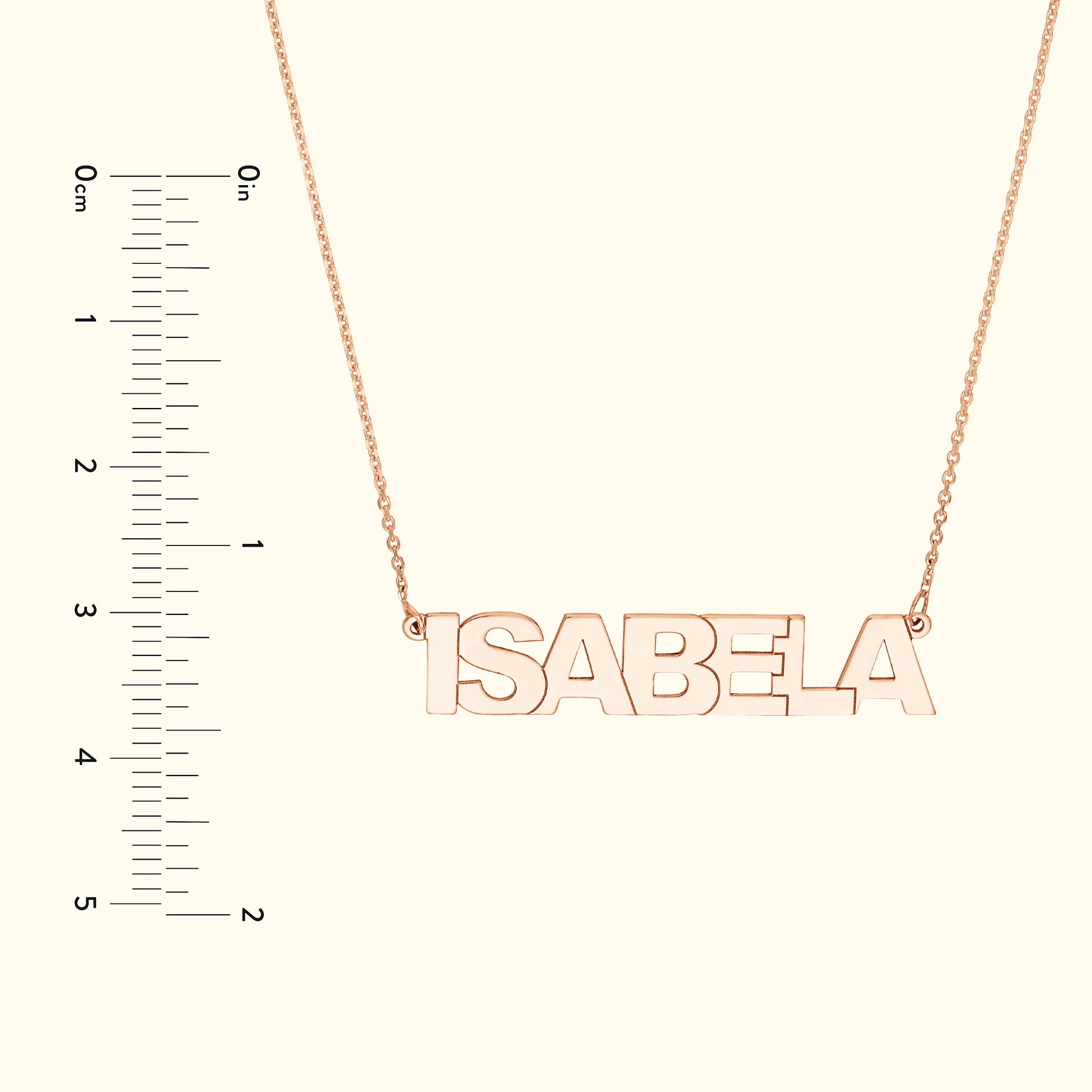 Rose gold necklace with the name "ISABELA" hanging on a delicate chain, alongside a ruler for size reference.