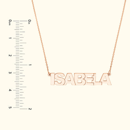 Rose gold necklace with the name "ISABELA" hanging on a delicate chain, alongside a ruler for size reference.