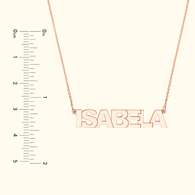 Rose gold necklace with the name "ISABELA" hanging on a delicate chain, alongside a ruler for size reference.