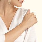 Delicate gold bracelet worn on a woman's wrist, with a soft white blouse in the background.